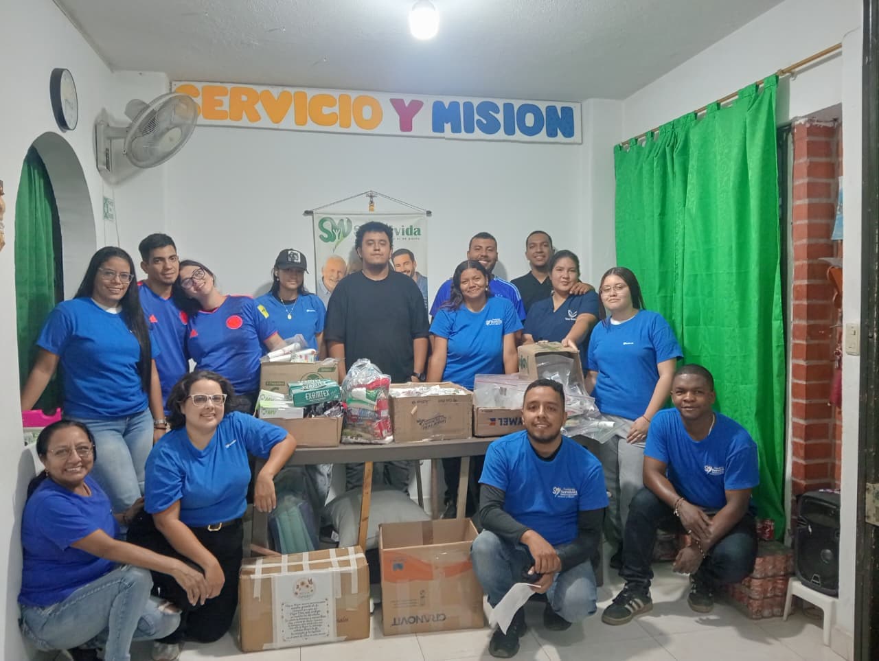 Equipo de voluntarios de la Fundación en la sede, con las donaciones ya clasificadas sobre la mesa y el letrero «Servicio y Misión» al fondo.